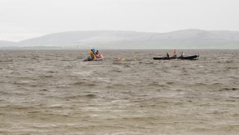 Support-crew-and-currach-boat-paddlers-in-open-ocean,-view-from-shoreline