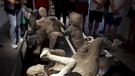 Plaster-Cast-Of-Citizens-of-Pompeii-On-Show-At-The-Antiquarium-With-Visitors-Standing-Around