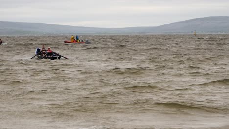 Pair-of-paddlers-row-currach-boat-out-to-open-ocean-sea-on-grey-stormy-day