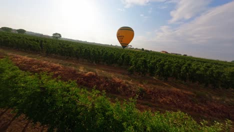 Epic-FPV-aerial-drone-flying-over-farm-fields-toward-a-hot-air-balloon