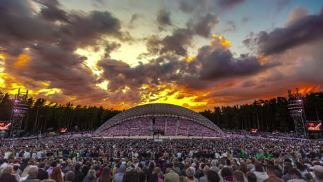 Toma-De-Tiempo-De-Una-Gran-Multitud-De-Personas-Reunidas-En-Un-Festival-De-Danza-Y-Canto-Letón-En-Un-Estadio-Al-Aire-Libre-En-Riga,-Letonia-En-Una-Noche-Nublada