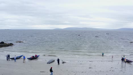 Drone-tilt-down-as-onlookers-spectate-and-walk-along-ladies-beach-galway-during-currach-festival