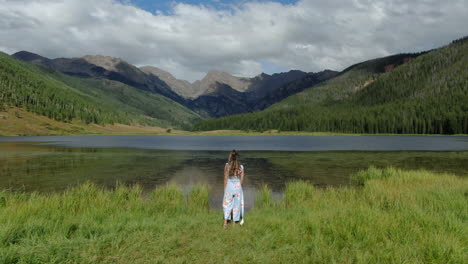 Aerial-cinematic-drone-circling-female-women-model-actress-cute-dress-walking-toward-Piney-Lake-Ranch-Vail-Beaver-Creek-Colorado-Gore-Range-mountain-landscape-windy-breeze-summer-rain-sun-clouds-calm