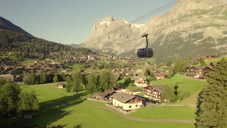 dolly-sideways-right-to-left-with-views-of-a-cabin-descending-on-tricable-car-system-Eiger-Express-in-front-of-Grindelwald-village-and-Mount-Wetterhorn