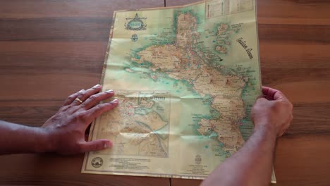 Mann-Hebt-Die-Karte-Der-Insel-Mahé-Auf-Den-Tisch,-Um-Die-Orte-Und-Sehenswürdigkeiten-Der-Insel,-Der-Seychellen,-Anzuzeigen