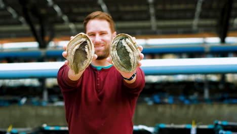 Caucasian-man-on-aquafarm-holds-out-two-farmed-South-African-abalone,-frontal