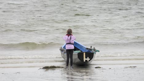 Young-female-child-prepares-to-enter-currach-boat-adjusting-life-jacket-facing-ocean