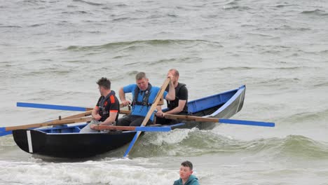 Group-of-three-men-rowing-currach-boat-attempt-to-launch-off-of-shore-in-ladies-beach