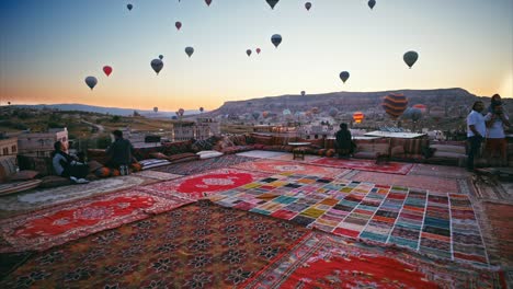 Tourists-on-the-roof-terrace-watching-the-balloons-floating-overhead-at-sunrise-in-Cappadocia