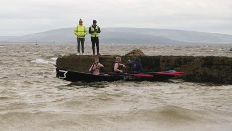 People-stand-at-watch-as-currach-boat-racers-paddle-oars-into-galway-bay