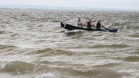 Group-of-racers-paddle-back-to-shore-catching-waves-and-crashing-on-sand-in-currach
