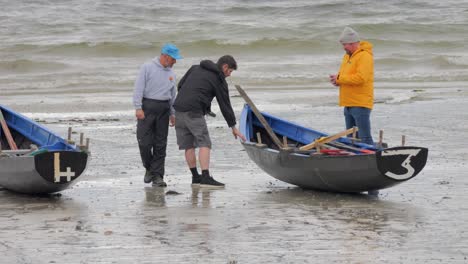 Men-stand-around-inspecting-curach-boats-on-the-shores-of-ladies-beach