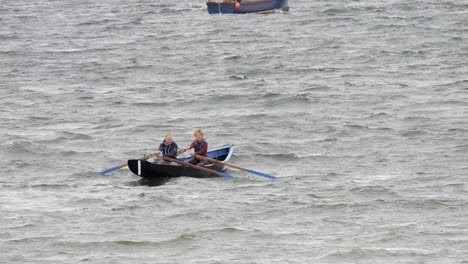 Slow-motion-view-of-couple-paddling-rowing-currach-boat-in-rocky-ocean