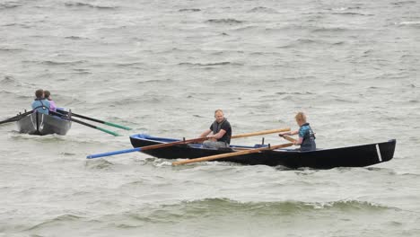 People-float-in-water-struggling-to-paddle-currach-boats-through-rough-seas