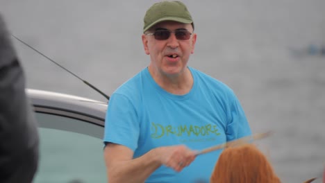 Older-irish-gentleman-leads-dance-and-hitting-of-drumsticks-by-the-beach-during-festival