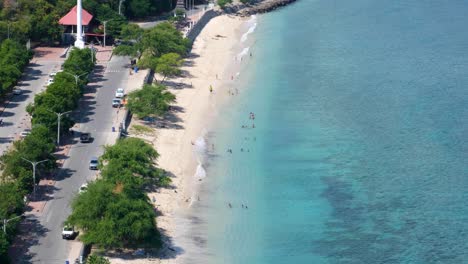 Aerial-landscape-view-of-people-in-Dili,-Timor-Leste,-enjoying-the-white-sandy-beach-and-swimming-in-crystal-clear-turquoise-ocean-water-at-Cristo-Rei