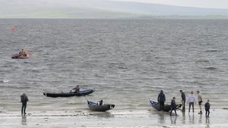 Slow-motion-of-solo-person-paddling-wooden-oars-from-currach-boat-with-county-clare-behind