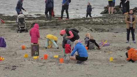 Wide-view-of-children-kids-and-parents-playing-and-building-sand-castles-on-the-beach-on-a-cold-day