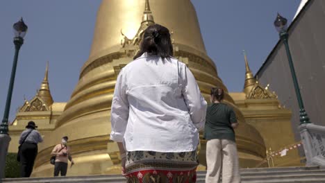 Slow-motion-shot-of-a-tourist-walking-up-the-steps-towards-a-golden-building-in-Bangkok