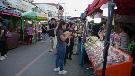 Touristen-Kaufen-Lebensmittel-Und-Machen-Ein-Paar-Fotos-Auf-Dem-Nachtmarkt,-Bevor-Sie-Eine-Bootsfahrt-Auf-Dem-Schwimmenden-Markt-Von-Amphawa-In-Thailand-Unternehmen