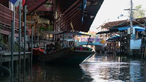 Zooming-in-to-a-boatman-who-is-paddling-a-wooden-boat-in-the-canal-of-Damoen-Saduak-Floating-Market,-Thailand