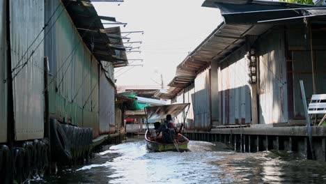 A-group-of-tourists-taking-a-boat-ride-in-a-wooden-boat-in-the-canal-of-Damoen-Saduak-Floating-Market,-Thailand