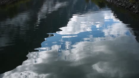 Nahaufnahme-Einer-Magischen-Wasseroberfläche,-Die-Einen-Blauen-Himmel-Mit-Wolken-In-Sanften-Wellen-Reflektiert