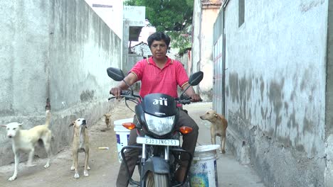 A-woman-running-an-NGO-is-taking-a-bike-on-a-village-road-distributing-food-to-hungry-dogs-and-cows