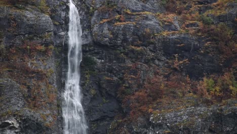 close-up-pan-over-a-massive-waterfall-over-a-rocky-cliff-with-autumn-colored-trees