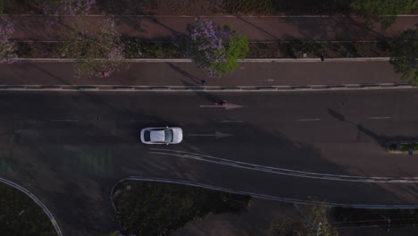 Aerial-tracking-overhead-view-white-car-drive-in-street-pass-pedestrian-crossing-main-road