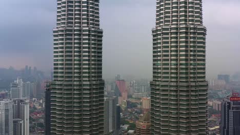 Aerial-drone-capturing-architectural-exterior-of-iconic-landmark-of-Malaysia,-Petronas-KLCC-Twins-towers-surrounded-by-downtown-cityscape-at-central-business-district,-Kuala-Lumpur-on-a-foggy-day
