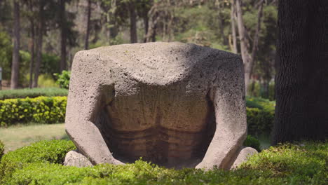 Die-Kopflose-Olmeken-Statue-Sitzt-Vor-Der-Kamera-Unter-Gesprenkeltem-Sonnenlicht-In-Einer-Bewaldeten-Landschaft,-Parque-Hundido,-Mexiko-Stadt