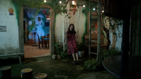 A-happy-Young-Asian-woman-swings-outside-her-home-at-night,-Wide-shot