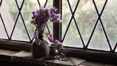 Vibrant-purple-flowers-arranged-in-a-rustic-vase,-placed-against-an-old-Victorian-window