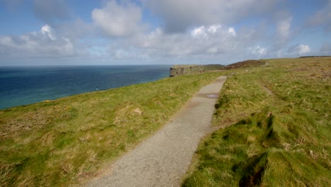 Extra-Wide-shot-of-sun-lilt-coastal-path-looking-at-Tintagel-cliffs-in-background,-from-Lower-Penhallic-Tregatta