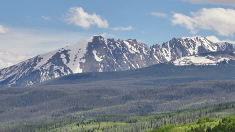 Sehr-Nahe-Luftaufnahme-Der-Wunderschönen-Colorado-Bergkette-Mit-Schneebedeckten-Gipfeln-An-Einem-Sonnigen-Tag-Mit-Blauem-Himmel-Im-Sommer-Mit-Grünen-Feldern,-Bäumen-Und-Berghäusern