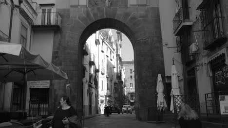 Black-and-white-tilt-down-shot-of-beautiful-historic-architecture-in-Naples,-Italy-with-tourists-and-locals-passing-by-on-a-sunny-day