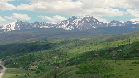 Nahaufnahme-Der-Wunderschönen-Colorado-Bergkette-Mit-Schneebedeckten-Gipfeln-An-Einem-Sonnigen-Tag-Mit-Blauem-Himmel-Im-Sommer-Mit-Grünen-Feldern,-Bäumen-Und-Berghäusern