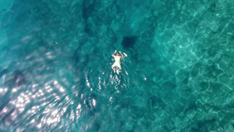 Drone-shot-of-a-tourist-man-snorkeling-in-crystal-clear-turquoise-ocean-water