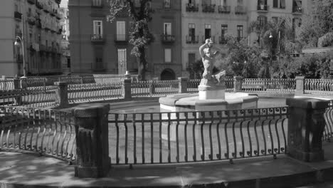 Black-and-white-shot-of-fountain-at-the-entrance-of-a-park-surrounded-by-residential-houses-in-the-historic-city-of-Naples,-Italy