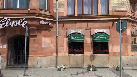 Elyse-Restaurant-entrance-in-Malmö:-Scandinavian-Culinary-Experience-and-Dining-Scene-in-Sweden's-Charming-Cityscape,-woman-walking-past-and-woman-cycling-past