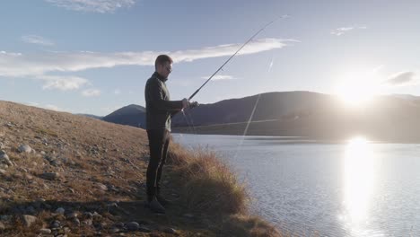 Young-fisherman-reeling-lure-back-in-during-sunset-above-mountains