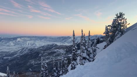 Tilt-up-shot-of-a-stunning-winter-landscape-scene-looking-down-at-a-cloudy-snow-covered-valley-during-a-golden-sunset-from-the-summit-of-a-ski-resort-in-the-Rocky-Mountains-of-Utah
