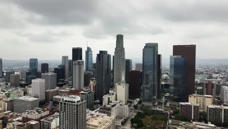 Corporate-skyline-of-LA-city,-dark,-overcast-day-in-USA---Descending,-drone-shot