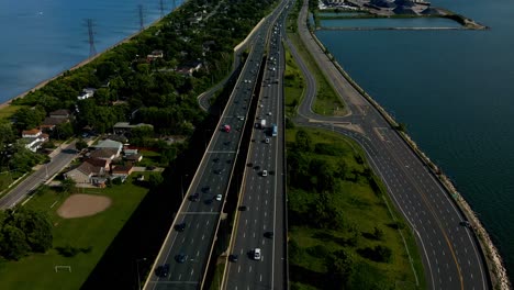 QEW-Burlington-to-Hamilton-reveal-drone-dolly-roll-birds-eye-top-view-to-skyline-landscape-view-of-light-traffic-as-4k60-filming-heads-into-downtown-core-blue-sky-at-Burlington-Harbor-sunny-summer-day