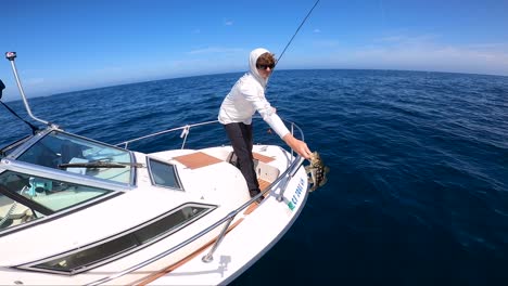 Young-fisherman-stands-at-bow-of-boat-holding-up-beautiful-calico-bass,-releases-catch-back-to-ocean