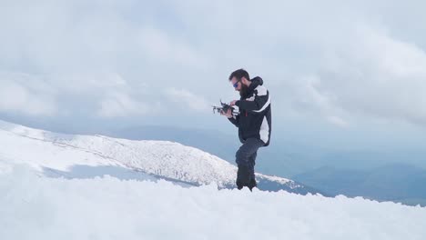 Man-standing-on-snow-covered-mountaintop-holding-drone-and-controller