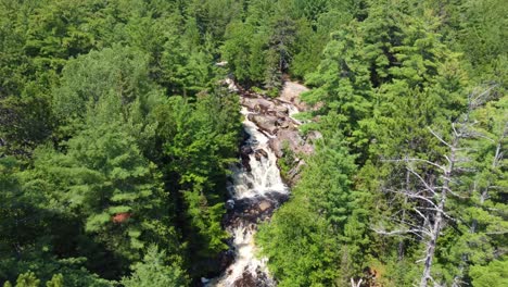 Drone-descend-tilt-up-establish-Duchesnay-Falls,-North-Bay-Ontario-Canada-hidden-behind-trees,-strong-flow-cascade-entire-waterfall