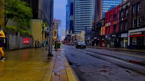 Yonge-Wellesley-wet-streets-after-rainfall-cyclists-deliver-food-summer-day-in-post-modern-futuristic-glass-mirrored-reflection-of-new-buildings-in-the-background-and-brick-buildings-in-the-front