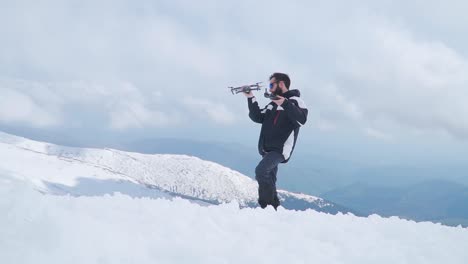 Bearded-man-standing-in-snow-on-top-of-mountain-holding-drone-makes-funny-face-and-shakes-head